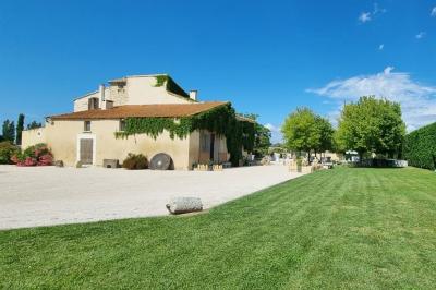 Bâtisse provençale entourée de cyprès et de champs verts, avec des arbres en arrière-plan sous un ciel clair.