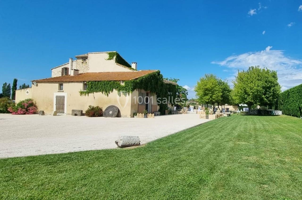 Bâtisse en pierre couverte de lierre, entourée d'une cour gravillonnée et d'une pelouse sous un ciel dégagé.