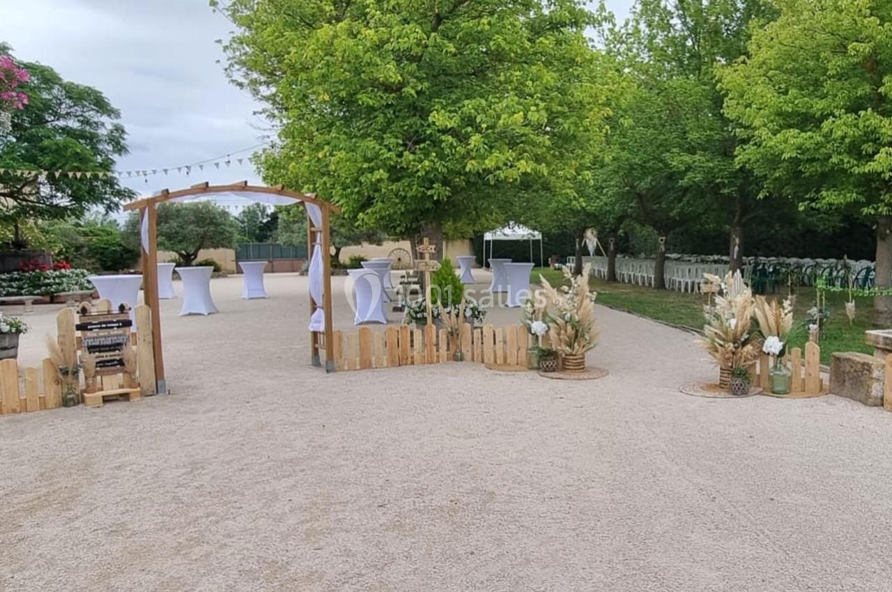 Espace extérieur décoré pour un événement, avec arche en bois, tables hautes et végétation environnante.
