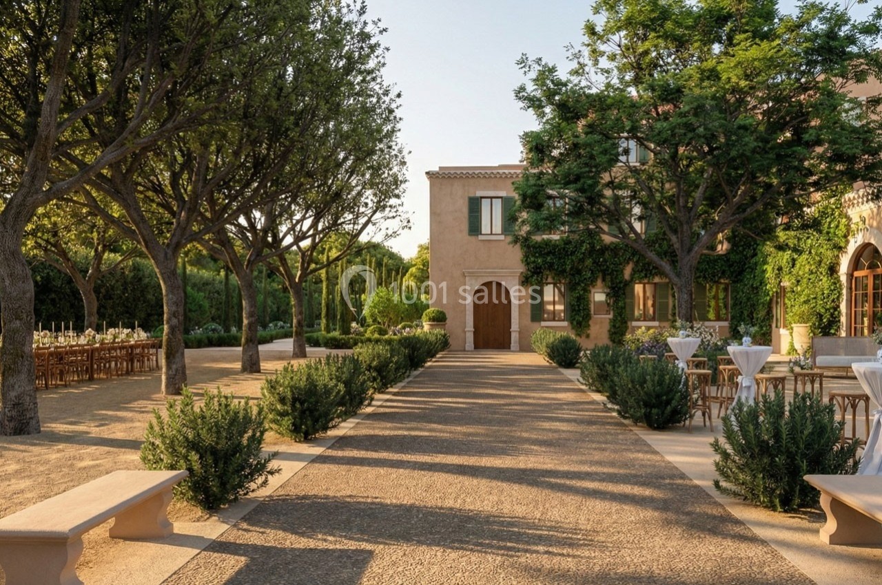 Allée bordée d'arbres menant à une bâtisse en pierre, avec tables dressées en extérieur sous un ciel dégagé.