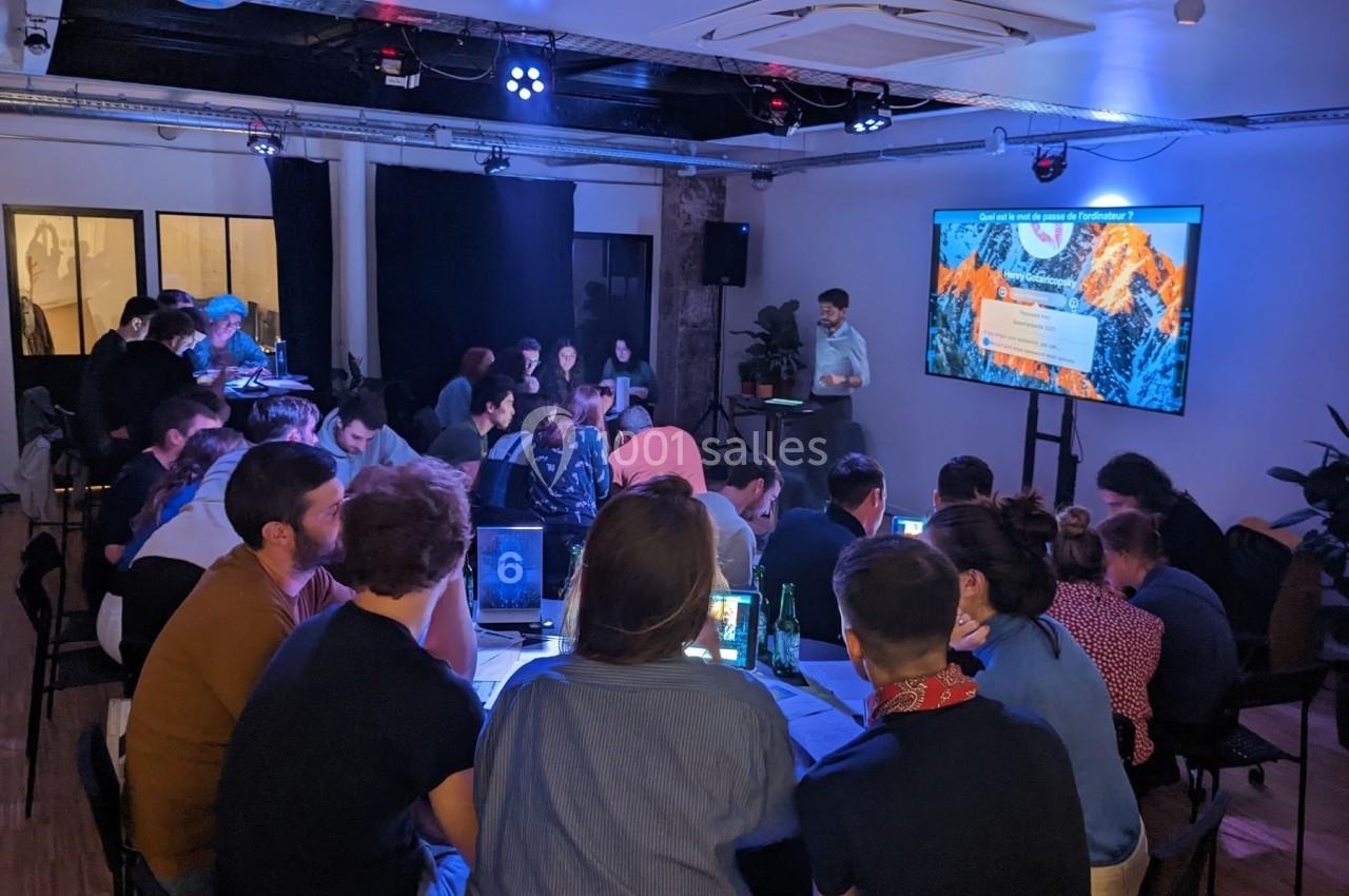 Un groupe de personnes assises autour de tables participe à une présentation projetée sur un écran dans une salle sombre.