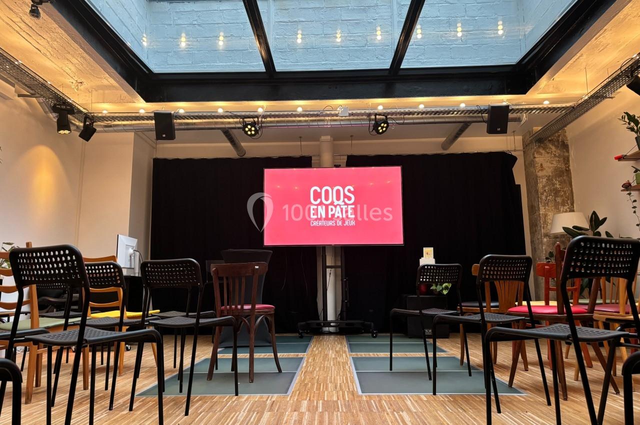 Salle lumineuse avec des chaises disposées face à un écran affichant ’Coqs en Pâte’ sous une verrière.