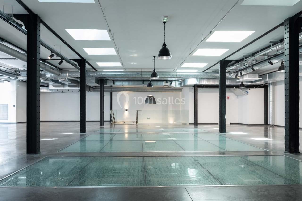 Intérieur d'un espace industriel moderne avec sol en verre, poutres métalliques et éclairage suspendu.