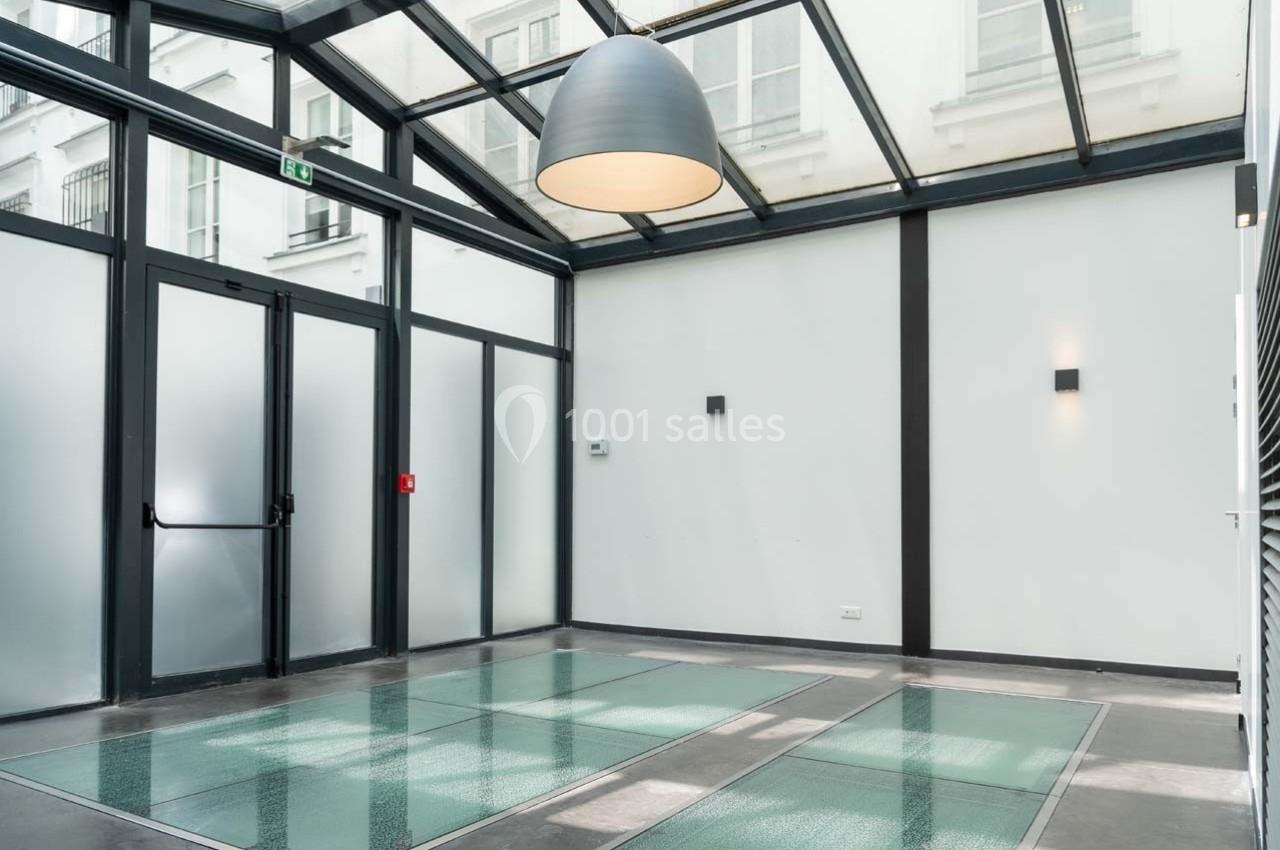 Salle lumineuse avec verrière, murs blancs, sol en verre et luminaires modernes.