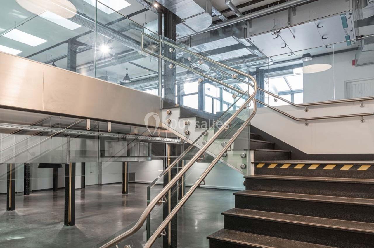 Escalier intérieur moderne avec garde-corps en métal et verre, dans un espace industriel lumineux.
