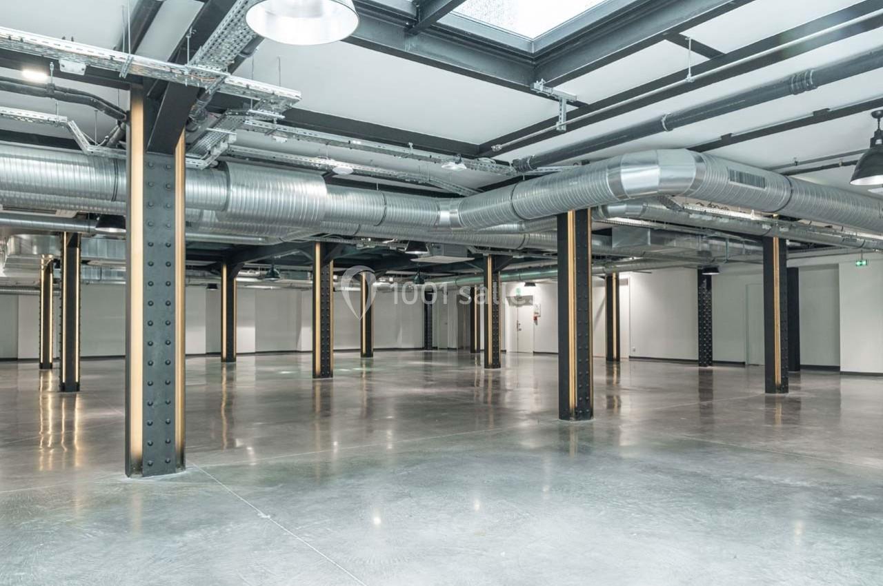 Intérieur d'un espace industriel vide avec sol en béton, poutres métalliques et conduits de ventilation apparents.