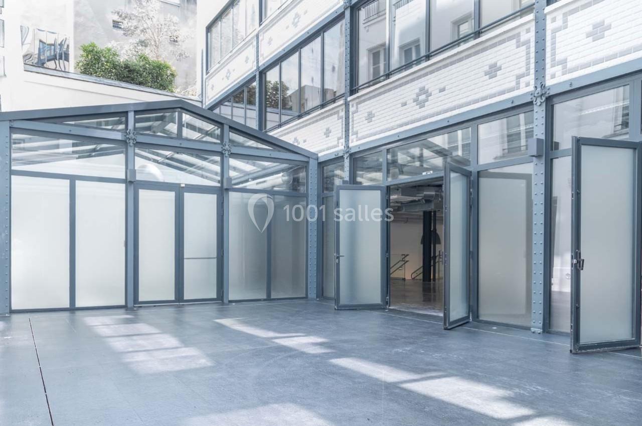 Cour intérieure moderne avec verrière, murs blancs en briques et grandes portes vitrées ouvertes.