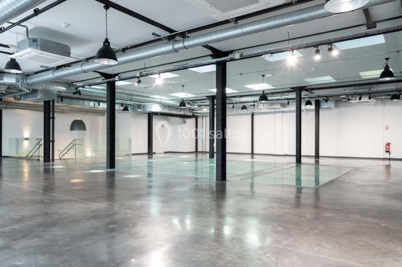 Intérieur d'un espace industriel rénové avec sol en béton, colonnes métalliques et éclairage suspendu.