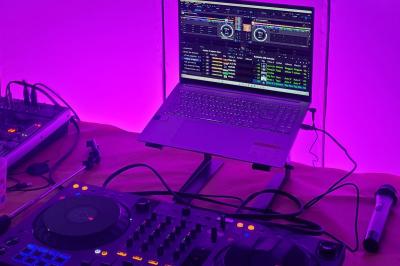 Poste de DJ avec une table de mixage, un ordinateur portable affichant un logiciel audio et un micro, éclairé en violet.