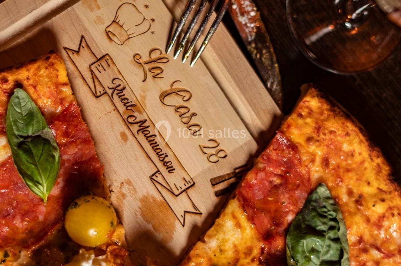 Deux parts de pizza garnies de basilic et tomates cerises sur une planche en bois gravée.