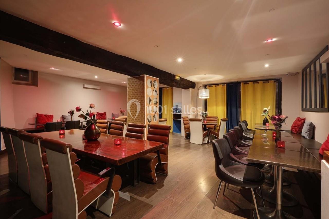 Salle de restaurant avec tables en bois, chaises rembourrées, éclairage tamisé et décoration florale.