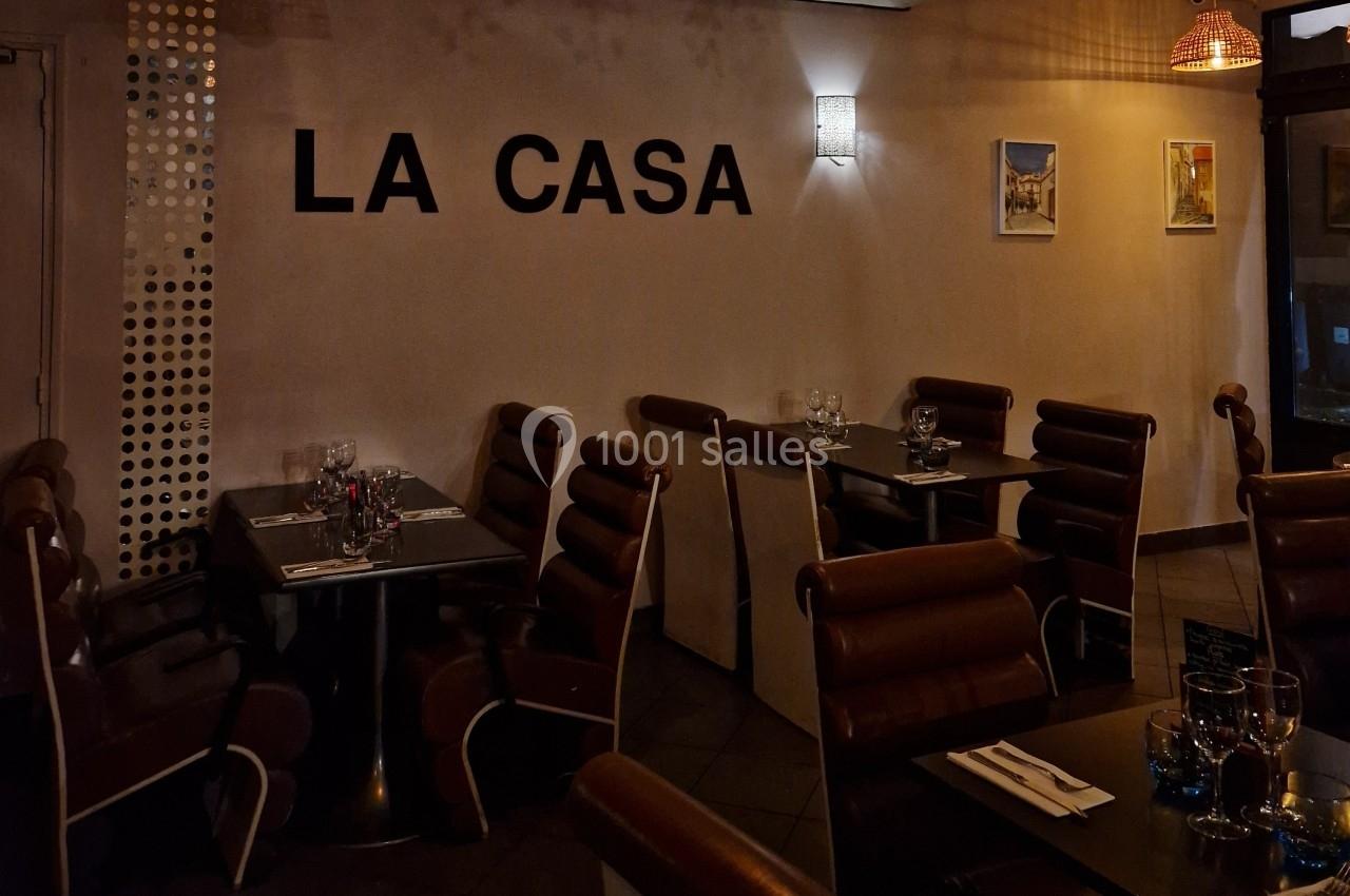 Salle de restaurant avec des tables dressées, des chaises en cuir marron et une enseigne murale ’LA CASA’.