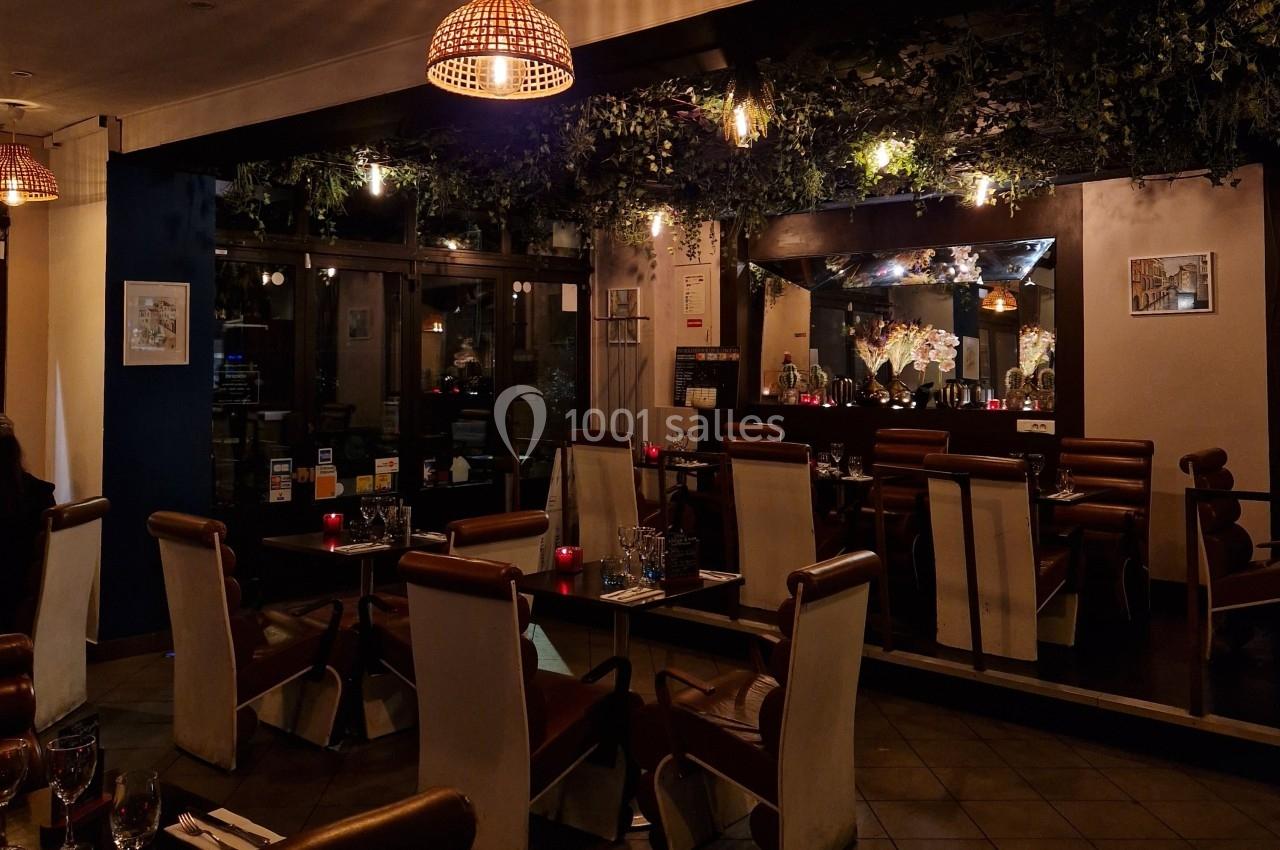 Salle de restaurant chaleureuse avec éclairage tamisé, tables dressées et décoration végétale au plafond.