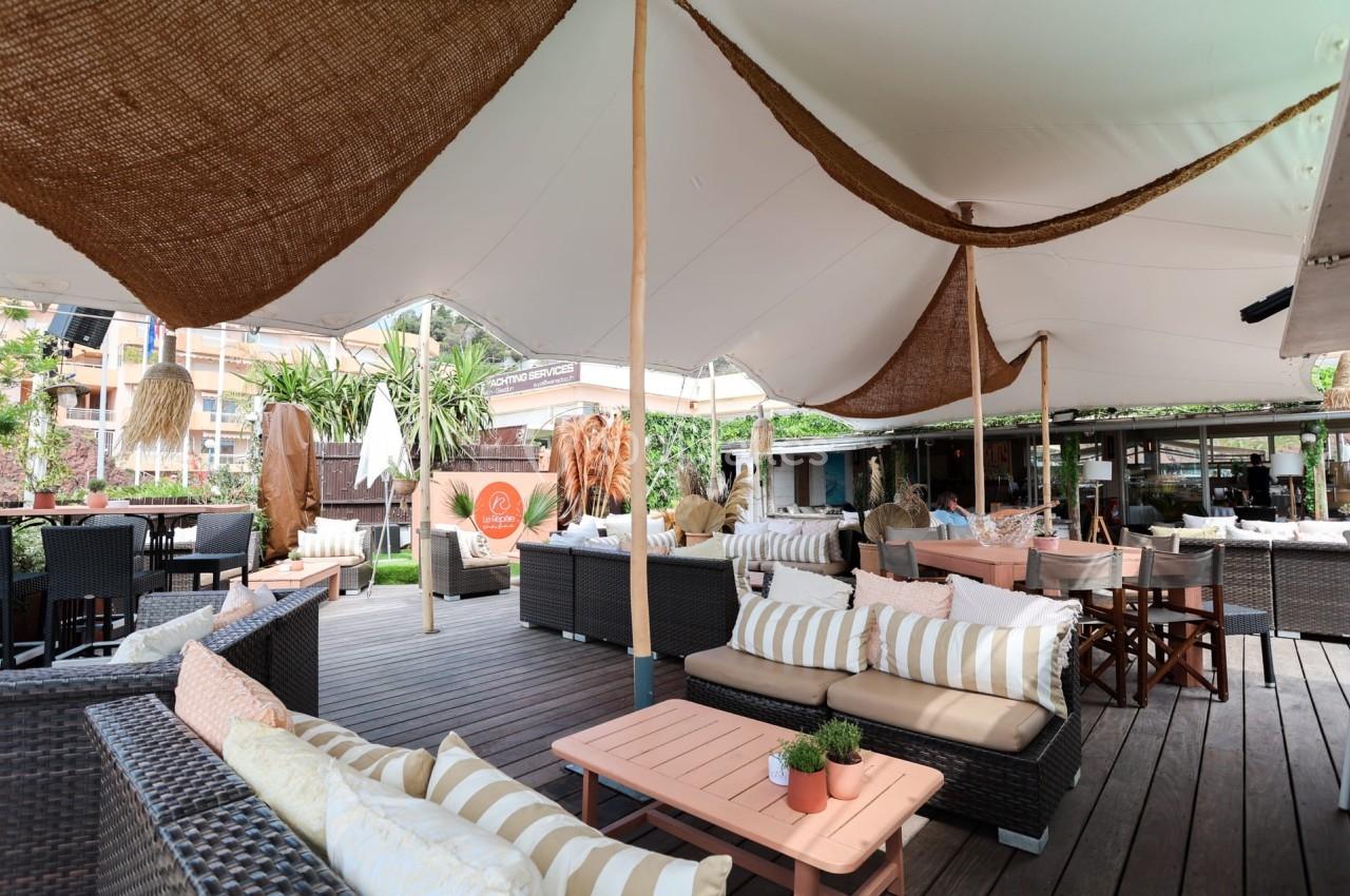 Terrasse extérieure aménagée avec des canapés, coussins rayés, tables basses et grande toile tendue pour l'ombrage.