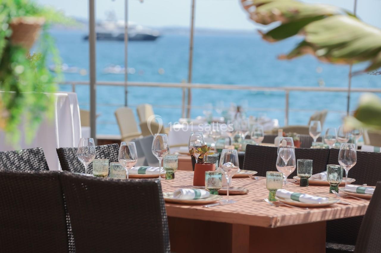 Table dressée en extérieur avec vaisselle élégante, vue sur la mer et un yacht à l'arrière-plan.