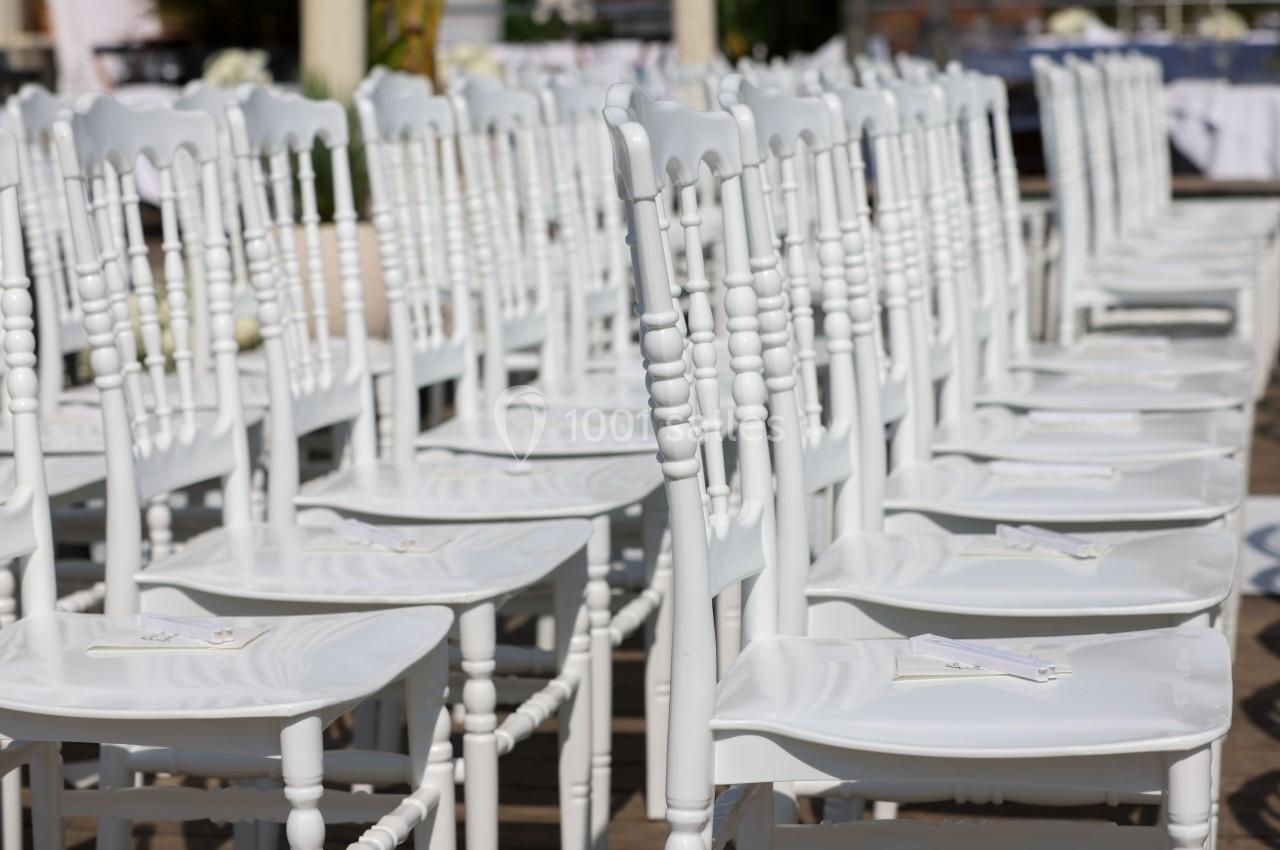 Rangées de chaises blanches alignées en extérieur, probablement pour un événement ou une cérémonie.