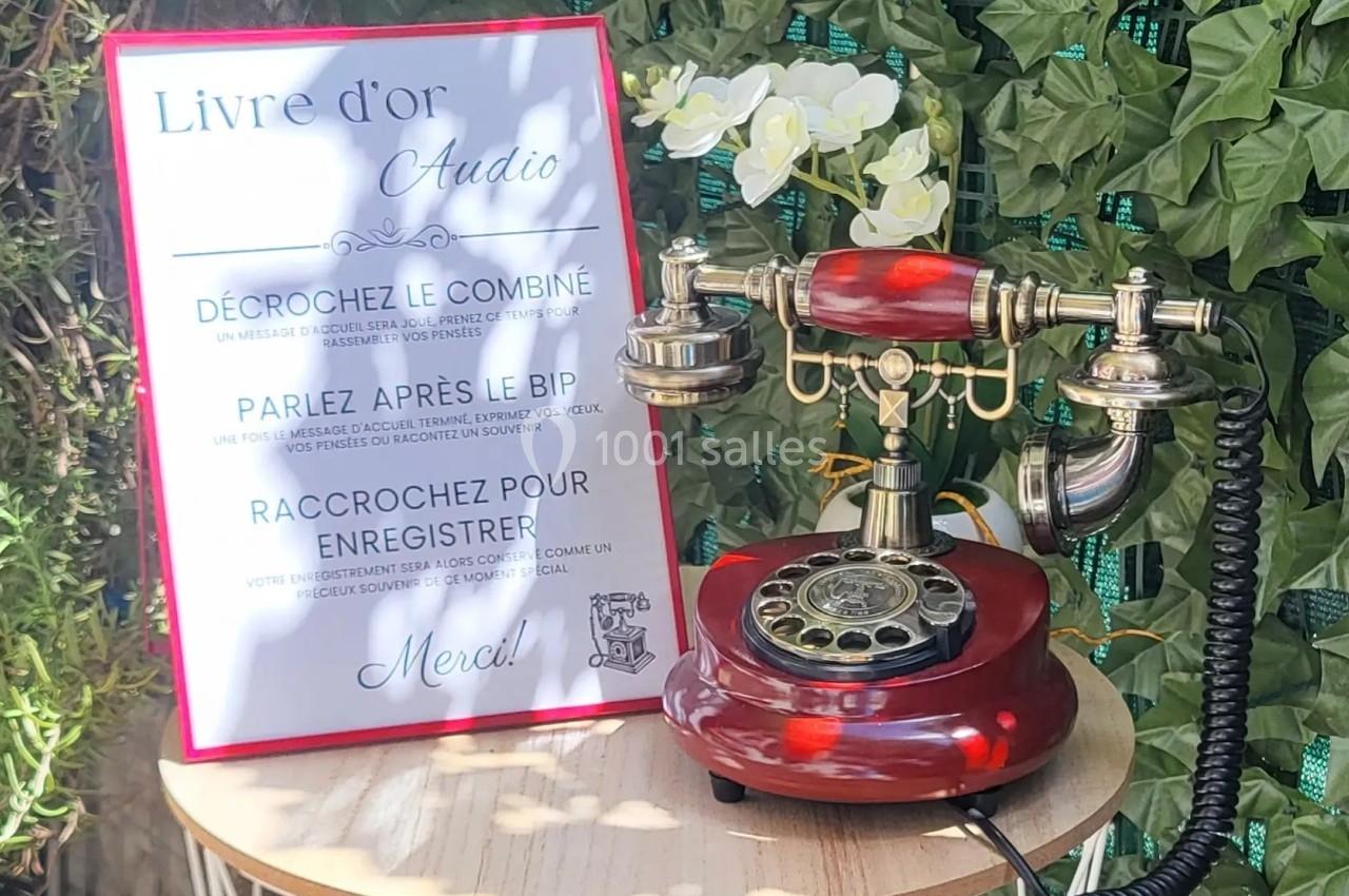 Téléphone rétro rouge avec cadran rotatif, posé sur une table près d'un panneau expliquant un ’livre d'or audio’.