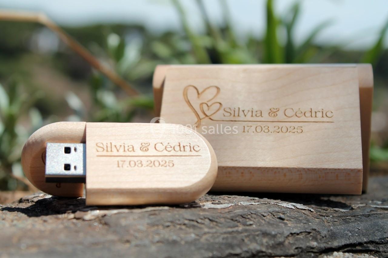 Clé USB en bois gravée avec les prénoms ’Silvia & Cédric’ et la date ’17.03.2025’, posée sur une surface naturelle.