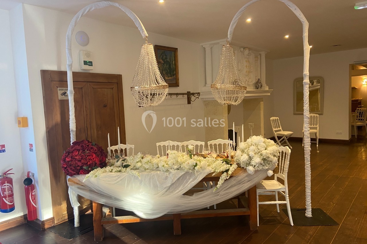 Table décorée pour un événement avec nappes blanches, fleurs rouges et blanches, chandeliers et chaises blanches.