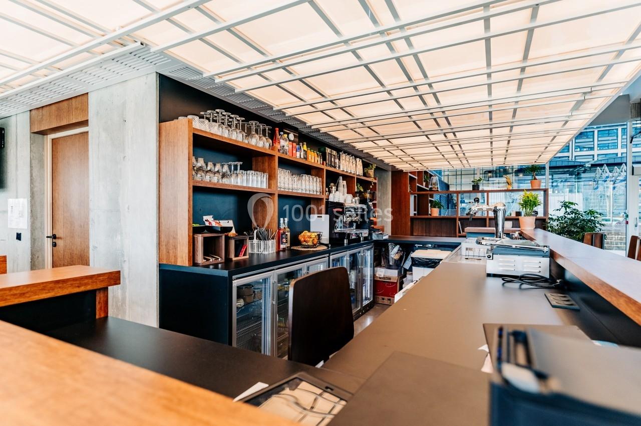 Comptoir de bar moderne avec étagères remplies de verres et bouteilles, éclairage lumineux au plafond.