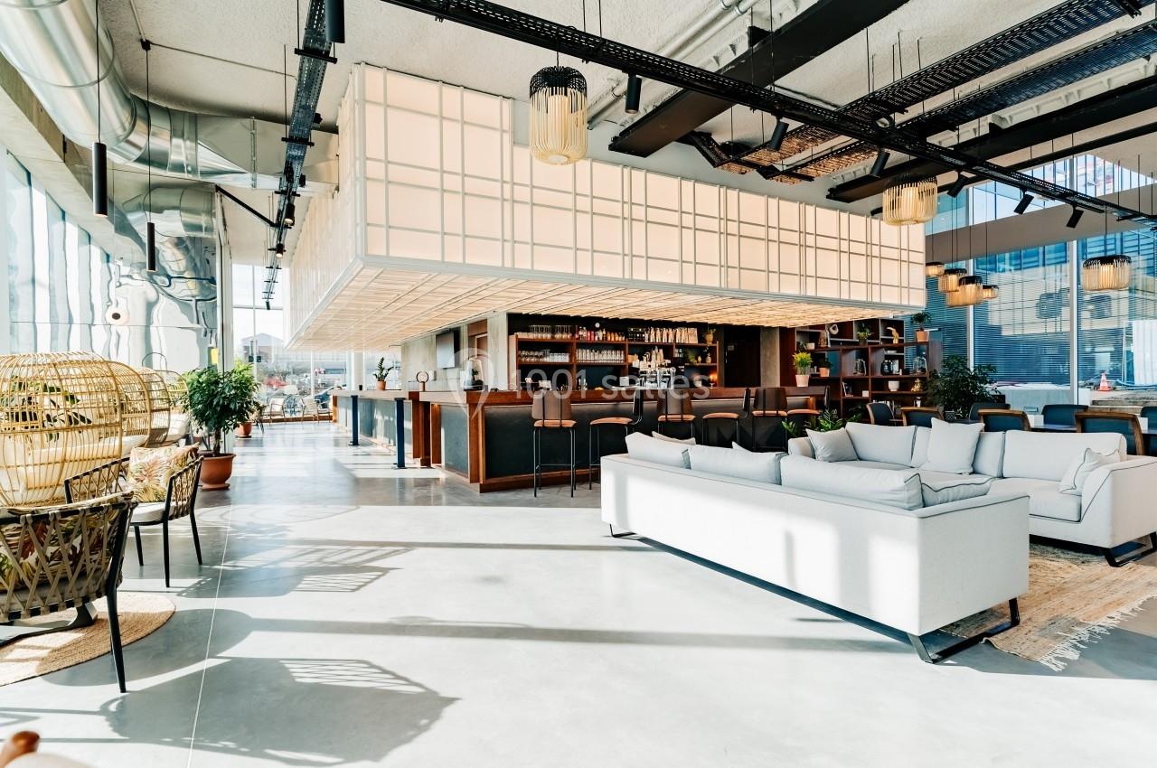 Espace lumineux avec un bar moderne, des canapés clairs et des plantes, dans un intérieur au design contemporain.