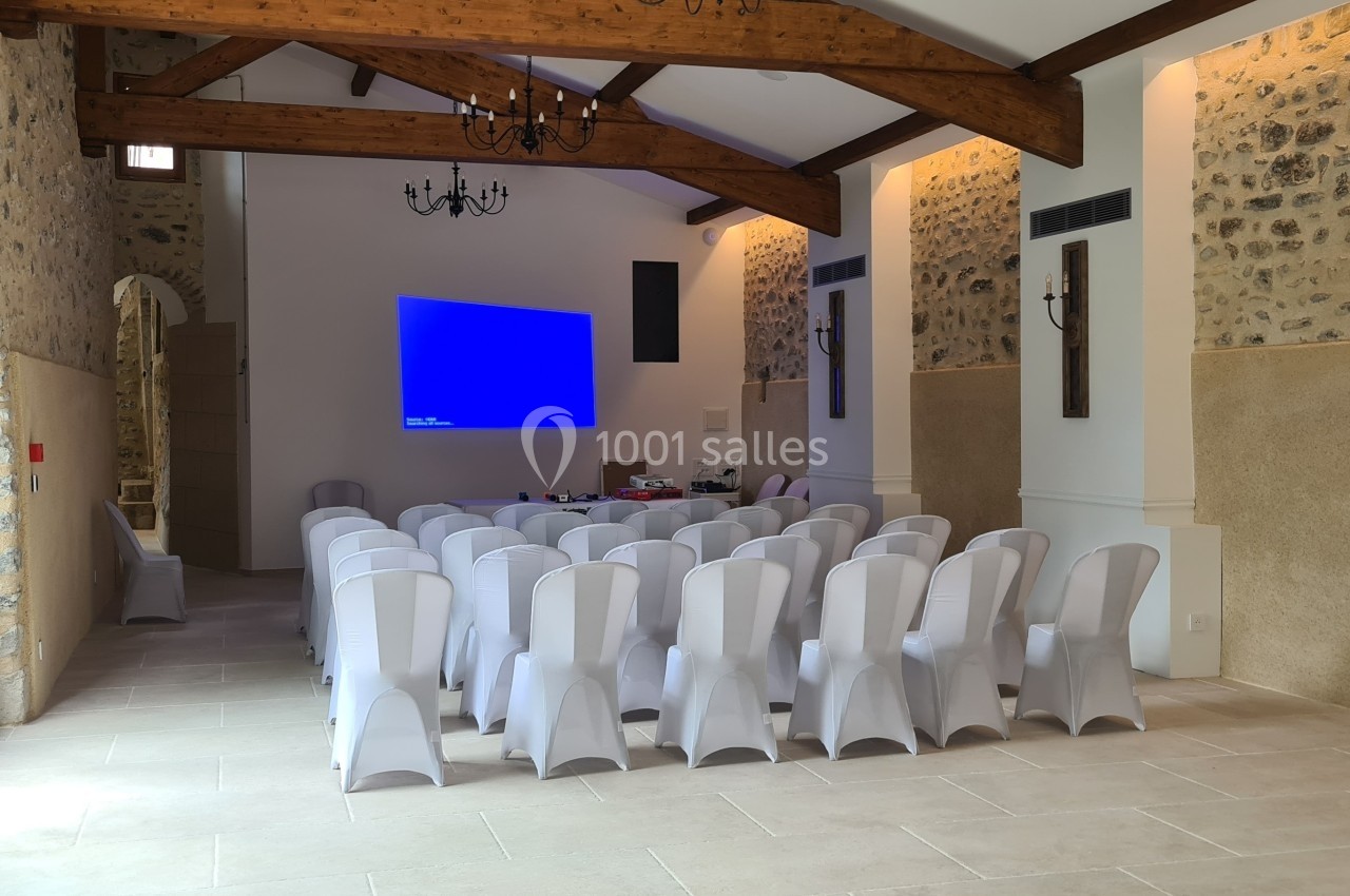 Salle de réunion lumineuse avec des chaises blanches alignées face à un écran de projection éteint.