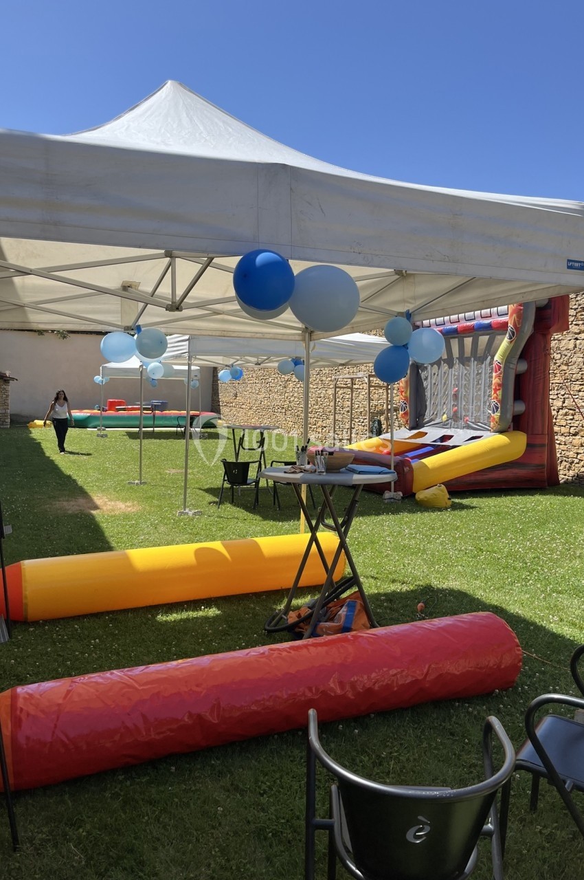 Espace extérieur avec tentes blanches, structures gonflables colorées et décorations de ballons bleus.
