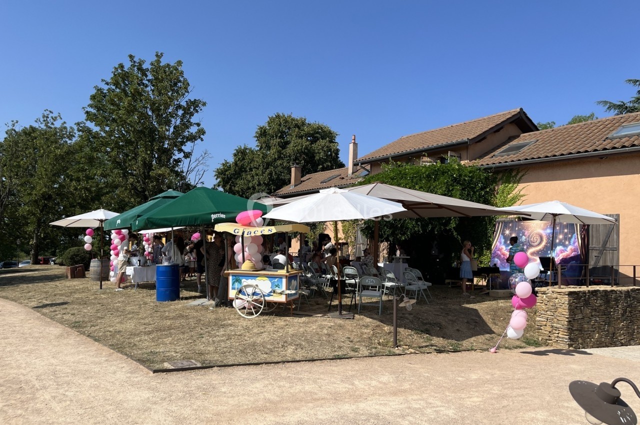 Des stands et des parasols installés en extérieur pour un événement, avec des décorations et des ballons roses.