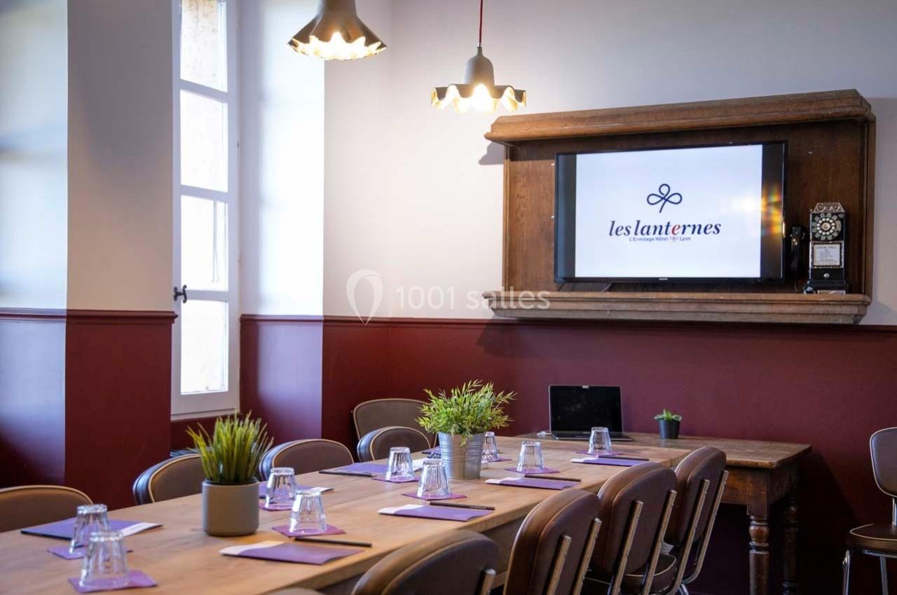 Salle de réunion lumineuse avec table en bois, chaises, plantes décoratives et écran affichant ’les lanternes’.