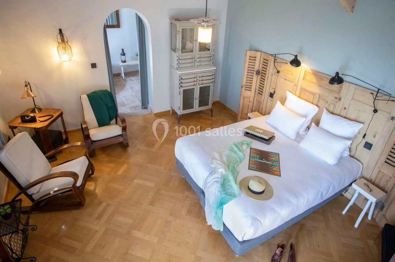Chambre lumineuse avec lit double, fauteuils en bois, parquet, armoire vintage et décoration chaleureuse.