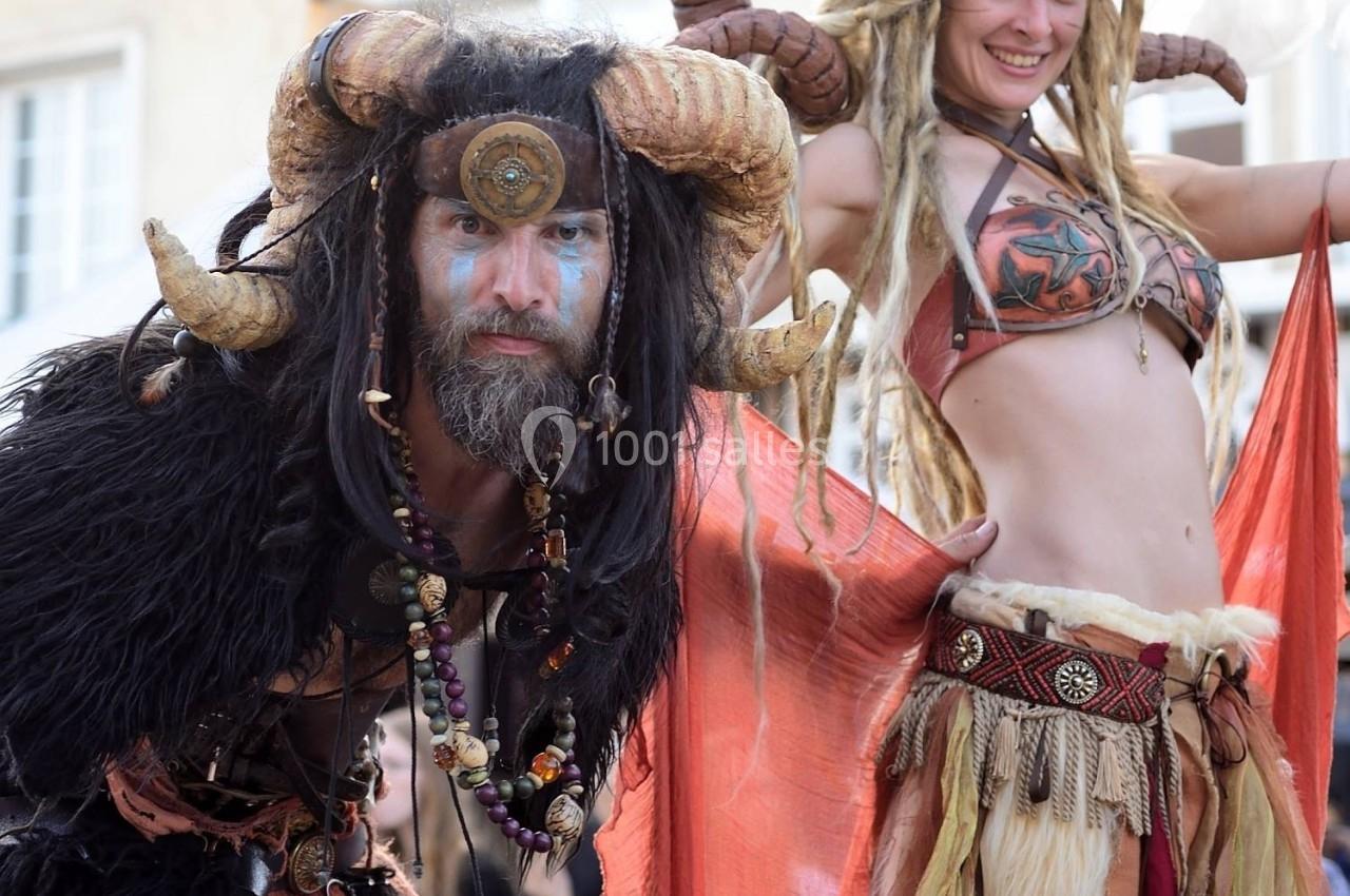 Deux personnes en costumes fantastiques avec cornes et vêtements ornés, posant dans une rue devant des bâtiments.