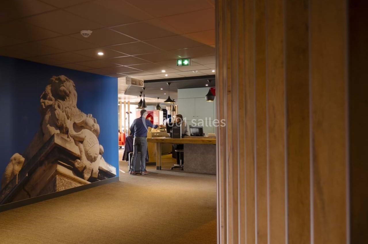 Accueil d'un bâtiment avec un comptoir, une personne en discussion et une fresque murale représentant une sculpture.