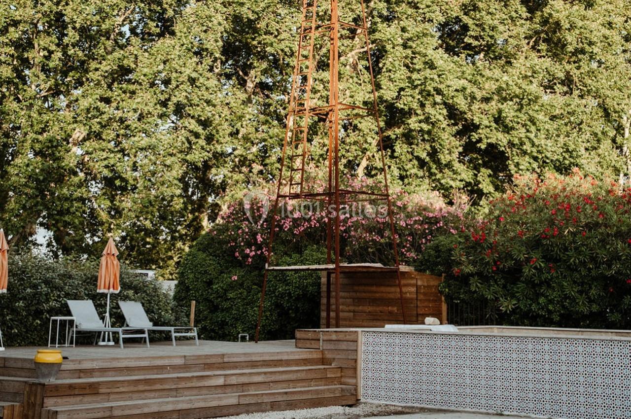 Terrasse en bois avec chaises longues, parasols rayés, piscine carrelée et végétation luxuriante en arrière-plan.