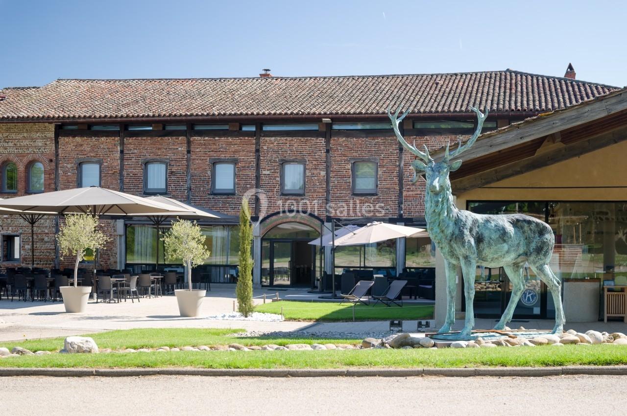 Statue de cerf en métal devant un bâtiment en briques avec terrasse aménagée et parasols.
