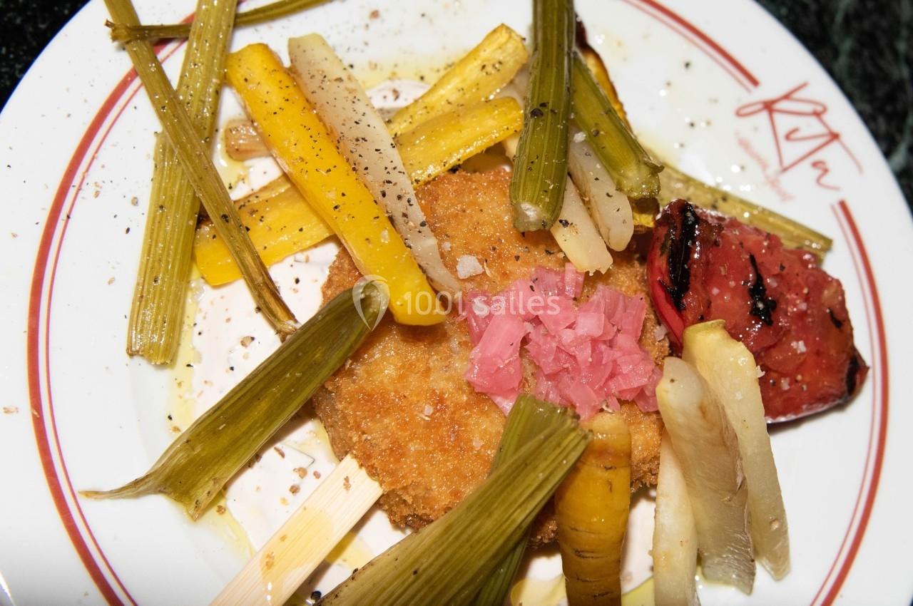 Assiette contenant un plat composé de légumes grillés, d'un aliment pané et d'une garniture rose sur le dessus.