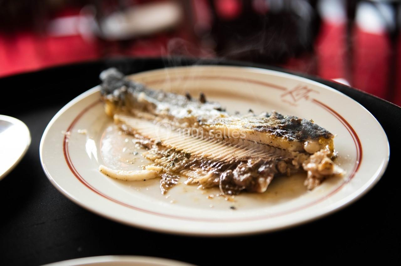 Assiette contenant un filet de poisson cuit, partiellement mangé, avec des arêtes visibles et un fond flou.