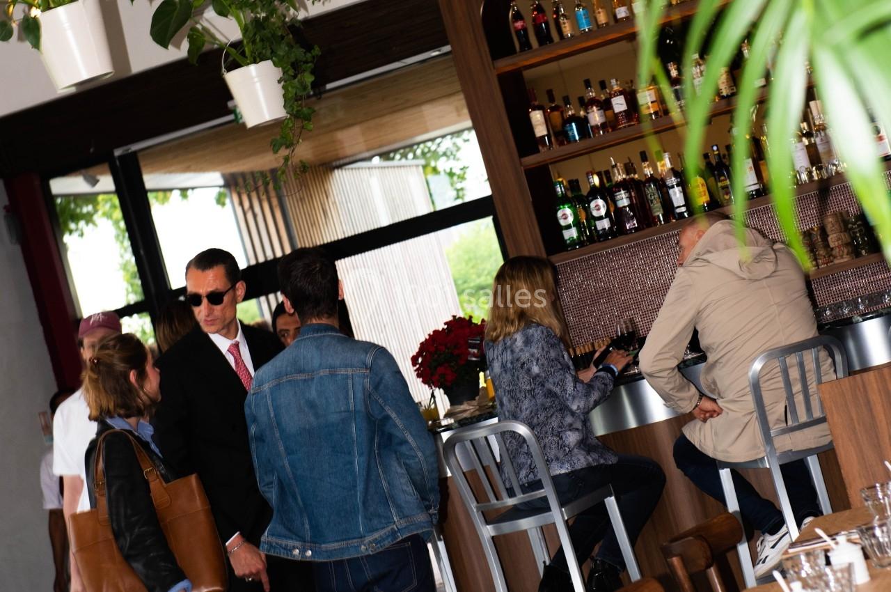 Des personnes discutent et prennent un verre au comptoir d'un bar moderne avec des étagères remplies de bouteilles.