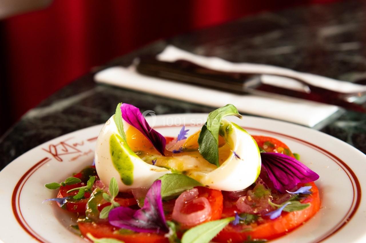 Assiette de salade composée de tomates, œuf dur, herbes fraîches et fleurs comestibles sur une table en marbre.