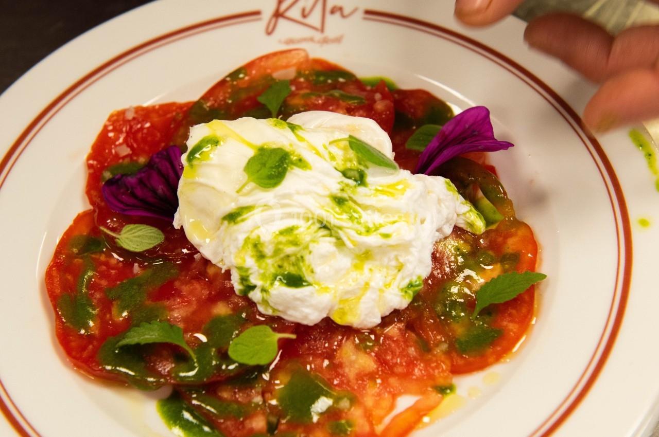 Assiette de carpaccio de tomates avec burrata, huile d'olive et herbes, décorée de pétales violets.