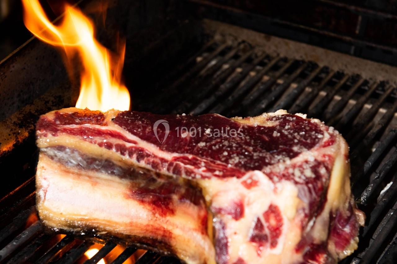 Morceau de viande épaisse en train de griller sur un barbecue, avec une flamme visible sur le côté.