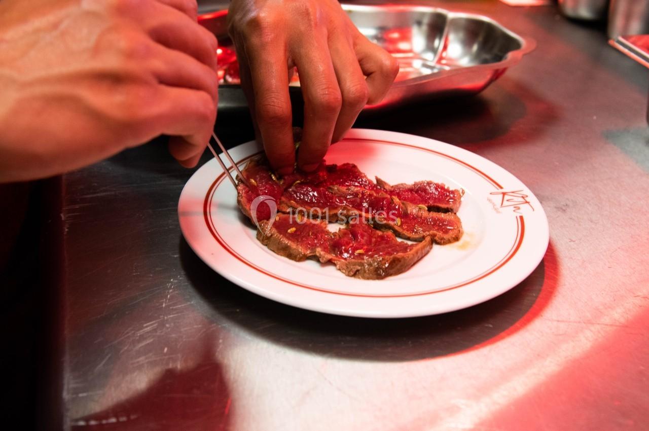Un chef dispose des tranches de viande crue sur une assiette blanche dans une cuisine professionnelle.