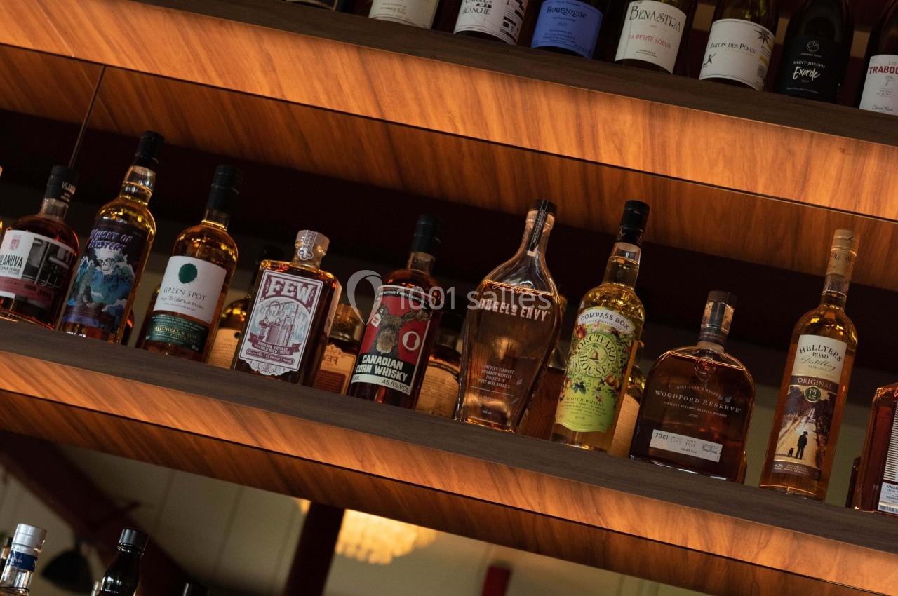 Bouteilles d'alcool variées disposées sur des étagères en bois dans un bar ou un restaurant.