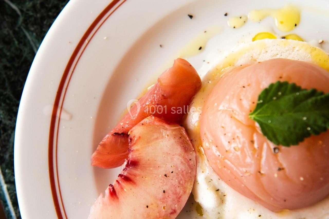 Une assiette contenant une pêche pochée sur un lit de ricotta, garnie d'huile d'olive et de feuilles de menthe.