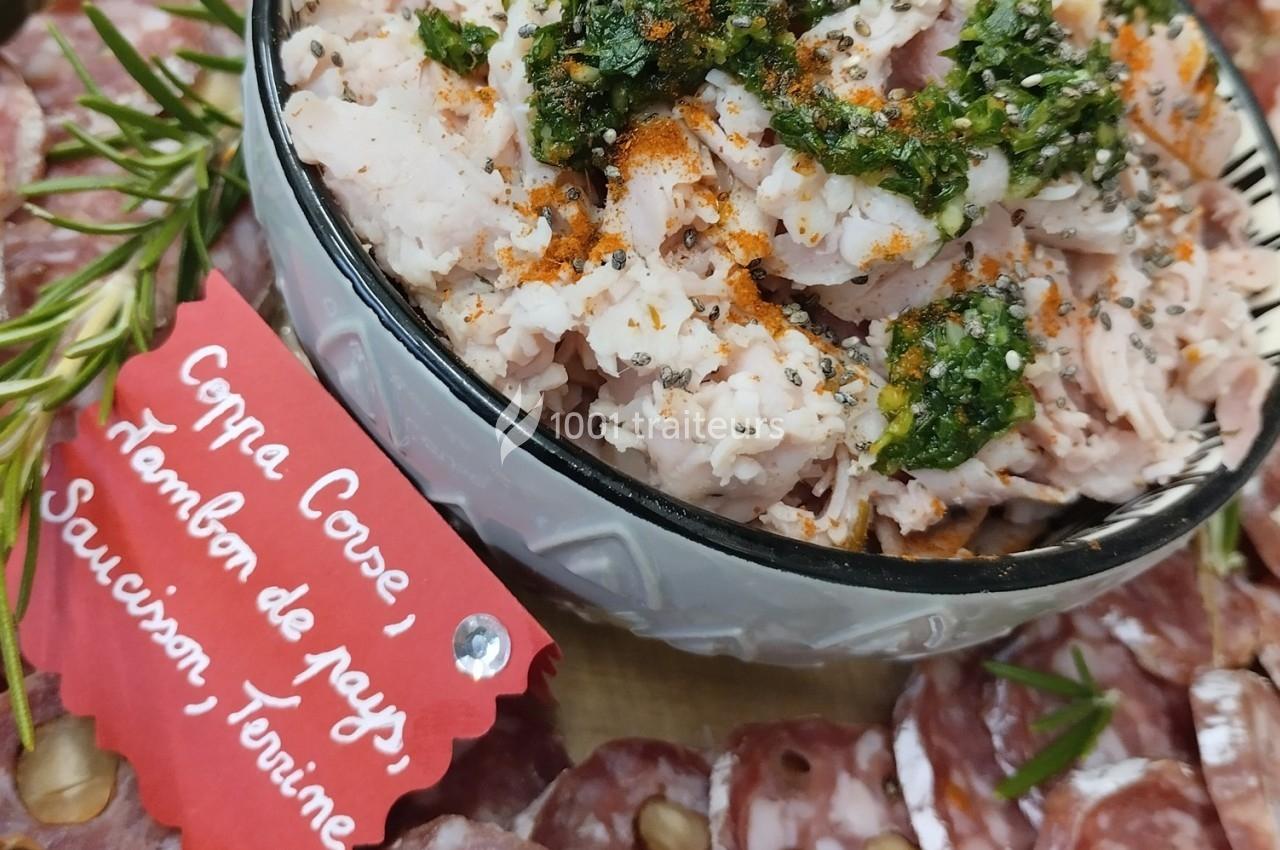 Assiette de charcuterie avec coppa, jambon, saucisson et terrine, garnie d'herbes et d'épices.