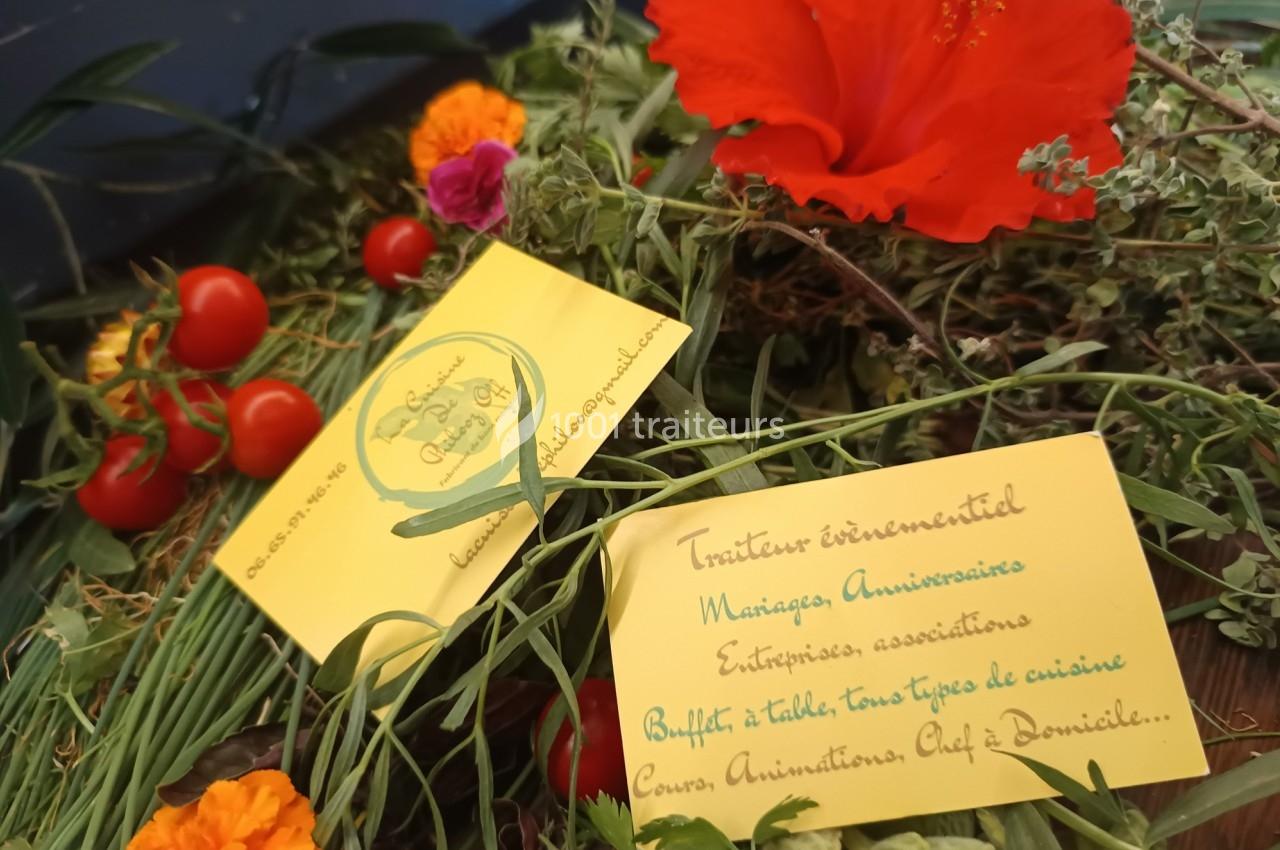 Cartes de visite d'un traiteur posées sur un mélange de fleurs, herbes et tomates cerises.