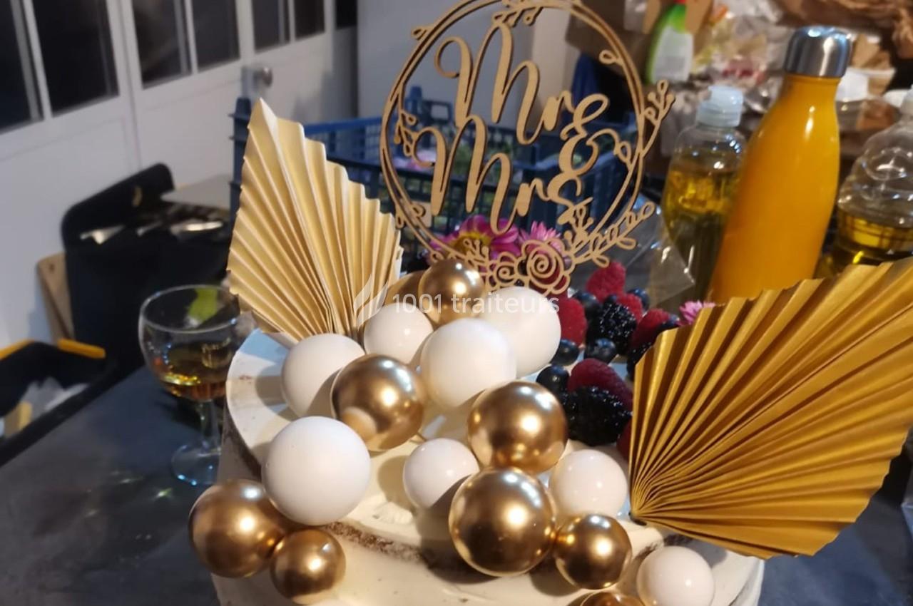 Gâteau décoré de perles dorées et blanches, éventails dorés et un topper ’Mr & Mrs’ sur une table.