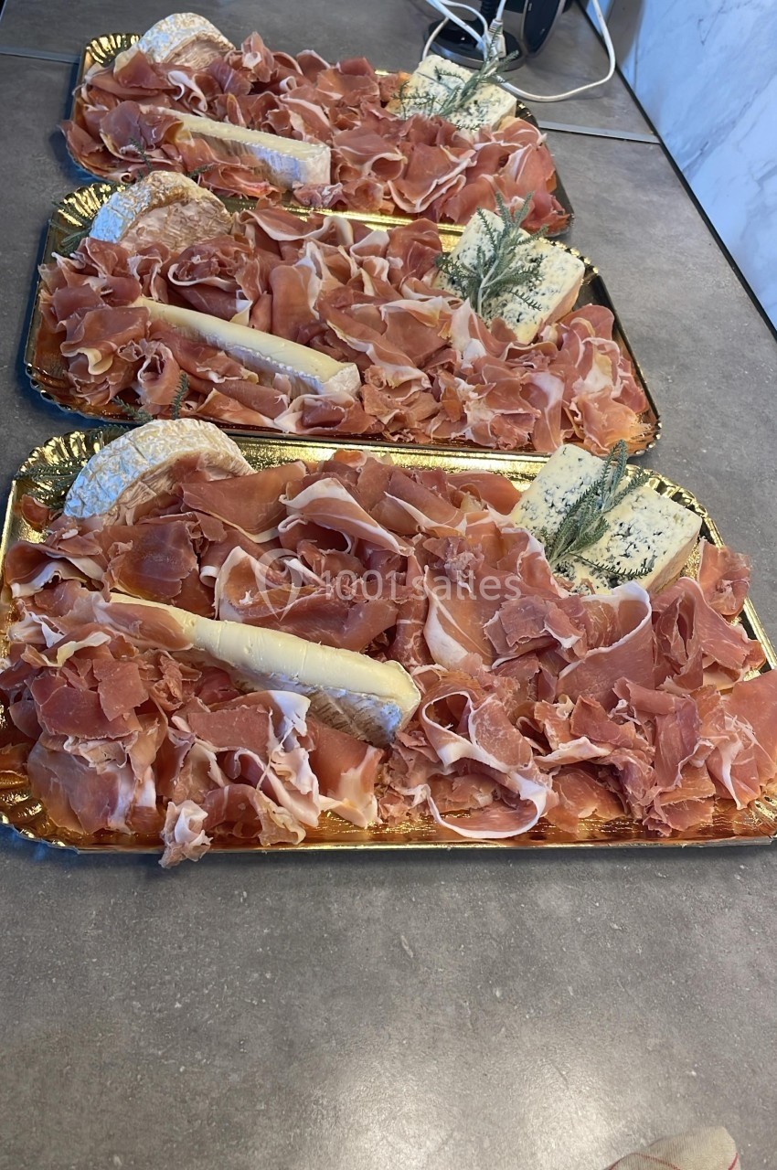 Plateaux de charcuterie avec tranches de jambon cru, fromage et brins de romarin sur un plan de travail.