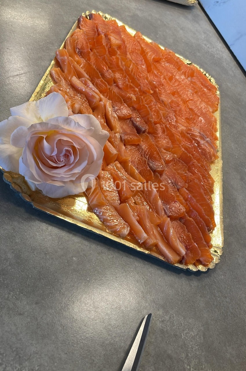 Plateau de tranches de saumon fumé disposées sur un plat doré, décoré d'une rose blanche.