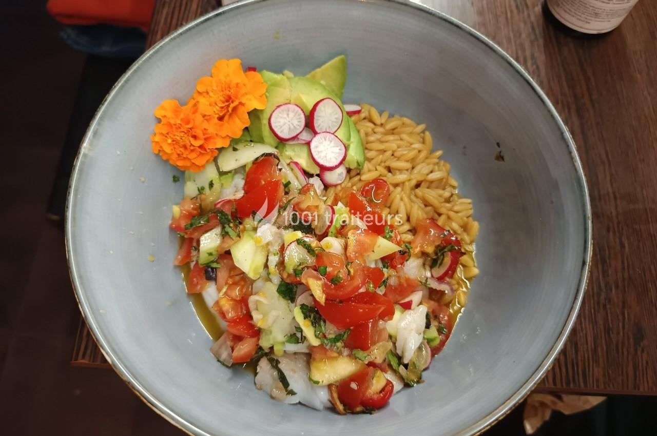Bol contenant un ceviche de poisson avec tomates, avocat, radis, orzo, fleurs comestibles et herbes fraîches.