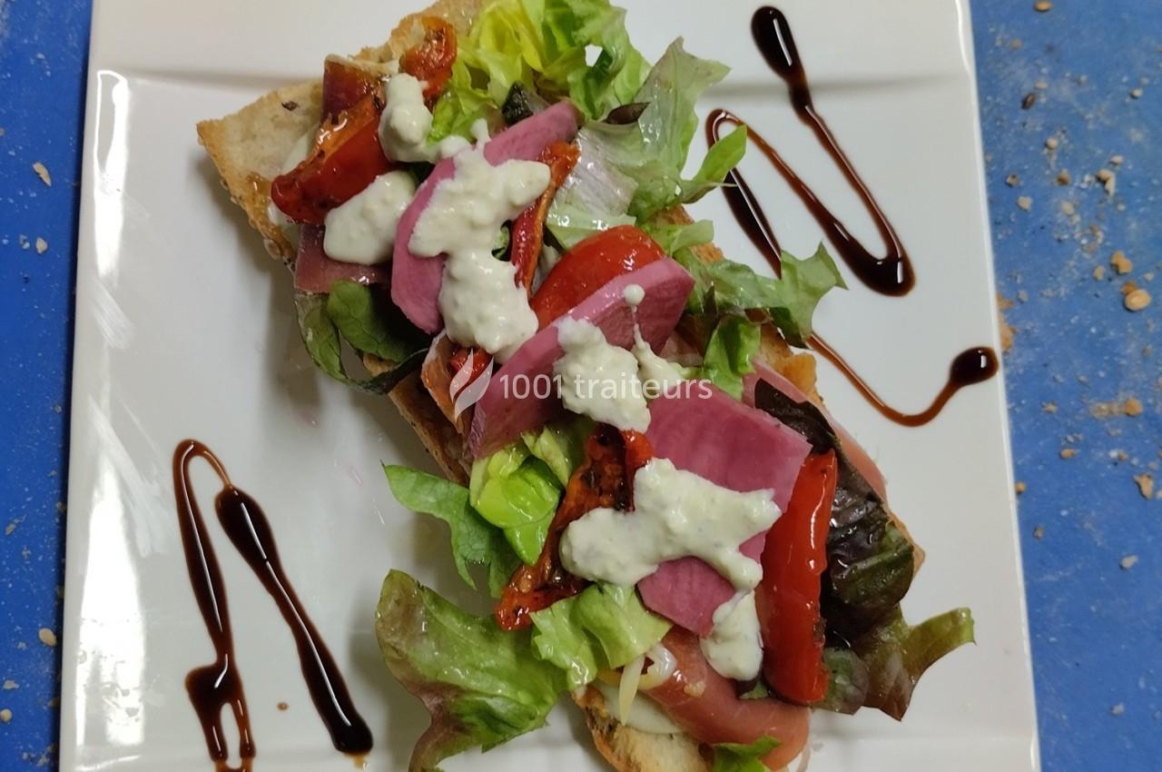 Tartine garnie de salade, légumes marinés, sauce blanche et filet de vinaigre balsamique sur assiette blanche.